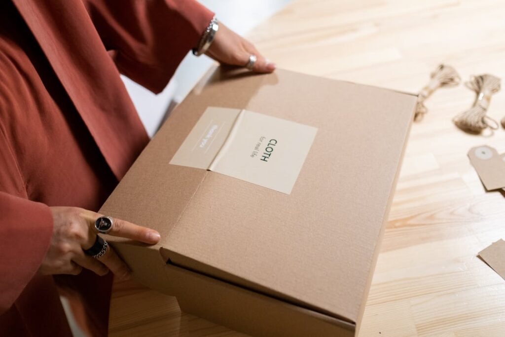 A person holding a brown box with a label named clothes.
