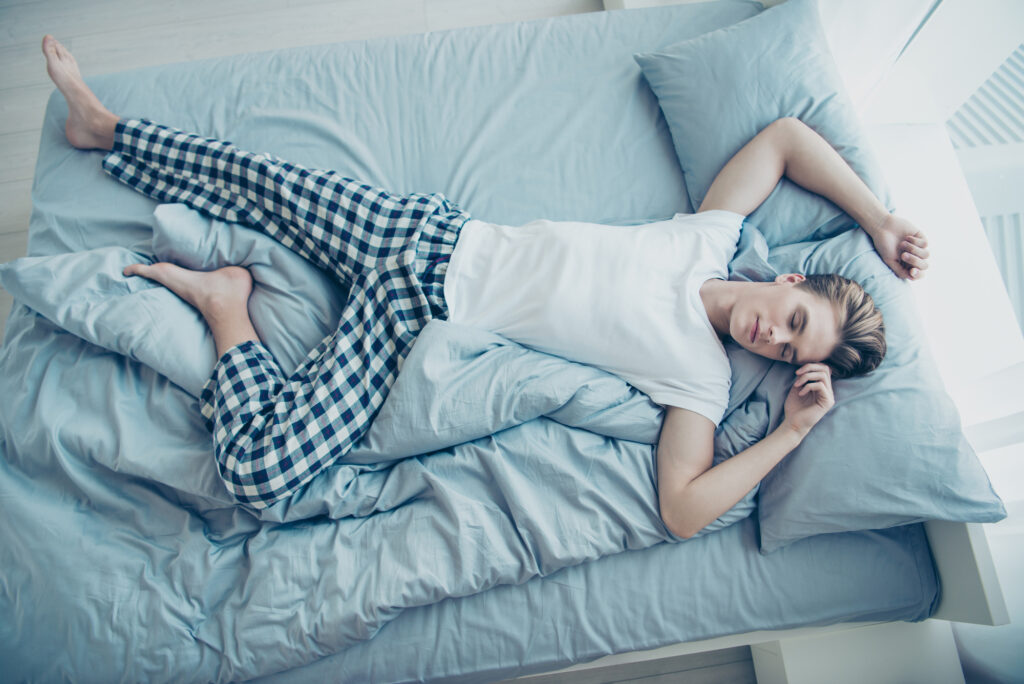 Top above high photo of dreamy calm man lying on bed sleeping on light blue sheets on his back have dreams, enjoy weekends free time wear checkered pajama in house indoors