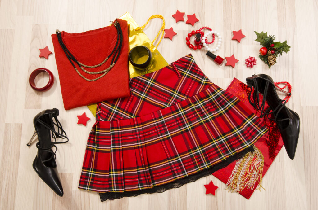 Woman red tartan plaid skirt outfit with matching, necklace, bracelet and nail polish lied down.