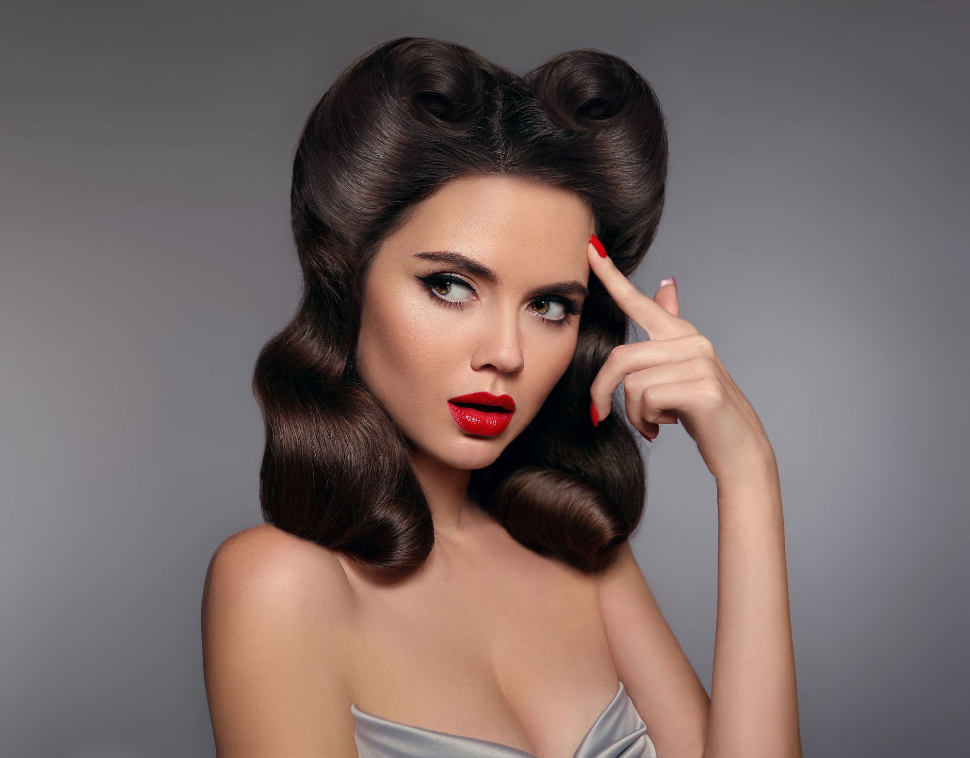 Pin up girl with red lips makeup and retro curls hair style. Retro woman looking to the side holds a finger near the head. Expressive facial expressions. High fashion photo.