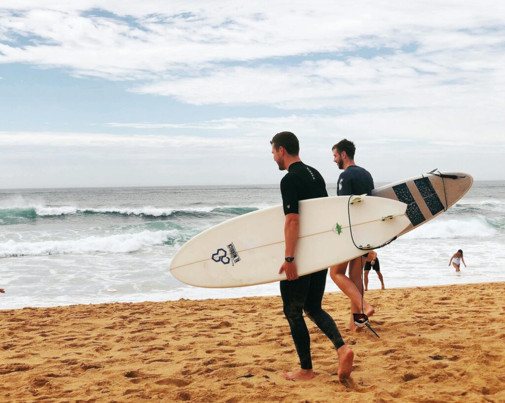 Two men carrying surfboards near the seashore.