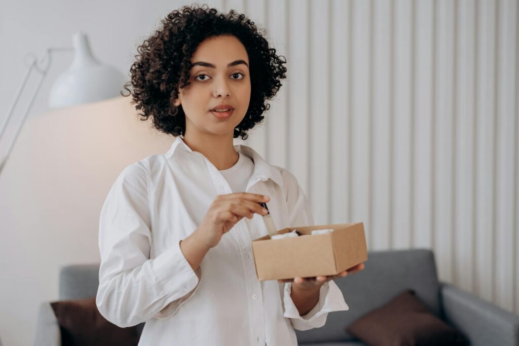 Young woman packing beauty products into a small box, demonstrating how to pack your cosmetics for a move efficiently