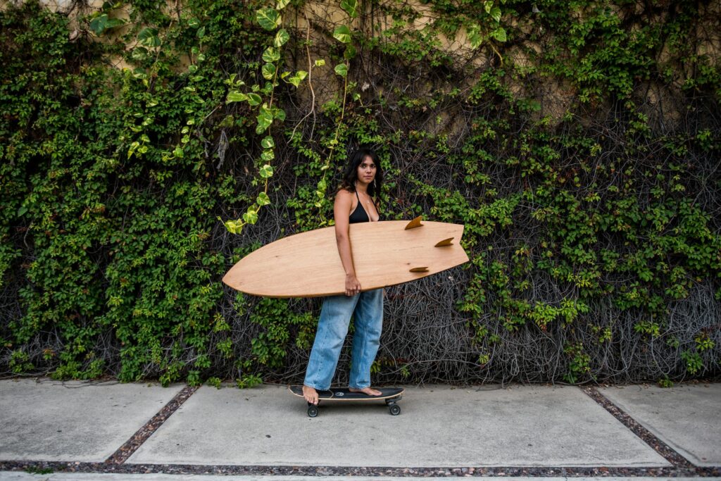 A woman with a surfboard near some greenery.