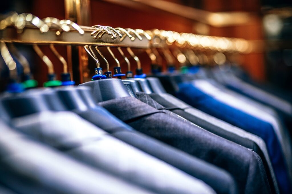 Row of neatly hung suits in various dark and neutral tones on golden hangers.