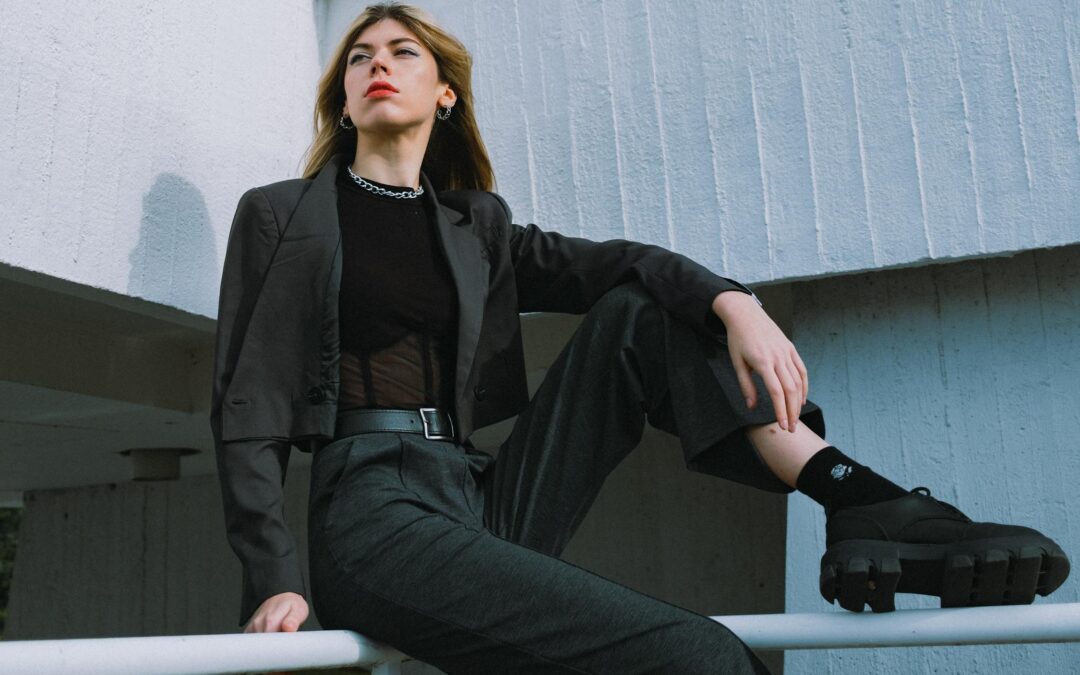 A stylish woman in a modern black suit poses confidently against a minimalist architectural background, embodying European fashion trends.